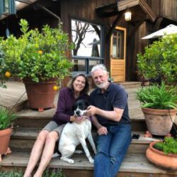 Dixie sitting one wide wooden steps with her new mom and dad on either side, with planters and citrus nearby