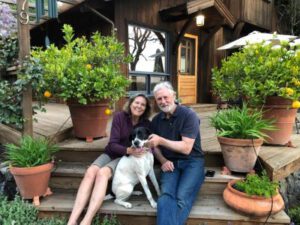 Dixie sitting one wide wooden steps with her new mom and dad on either side, with planters and citrus nearby