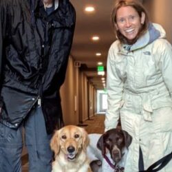 Remington next to his golden retriever sibling, with new dad and mom in raincoats in a hallway
