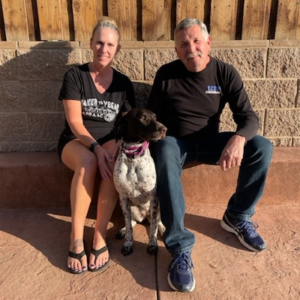 Lady3 sitting in front of block and wood fence with her new mom and dad