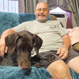Hudson on the coach with a paw on his new adoptive dad's leg